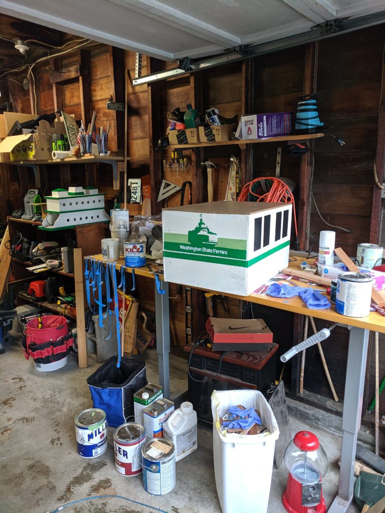 A picture of a box painted to look like a ferry terminal in a cluttered garage.